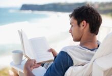 Man with coffee cup reading book in deck chair overlooking ocean 97970758 2122x1415 e1537973987850