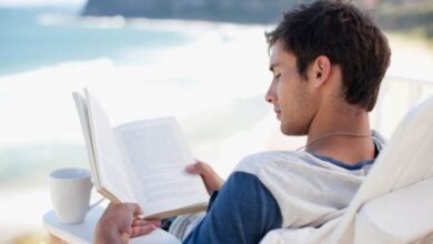 Man with coffee cup reading book in deck chair overlooking ocean 97970758 2122x1415 e1537973987850